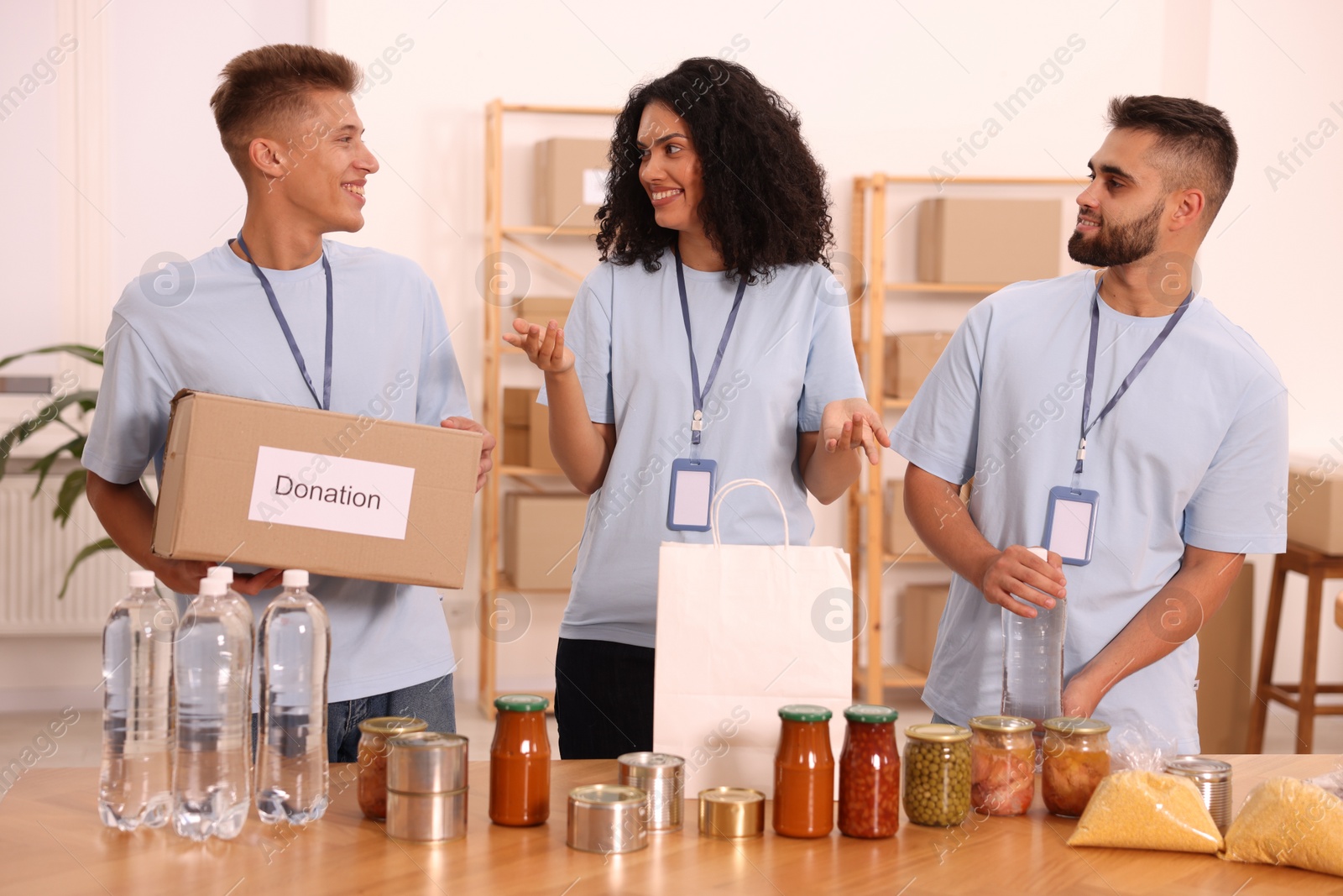 Photo of Group of volunteers with donation box, paper bag and food products at table in warehouse