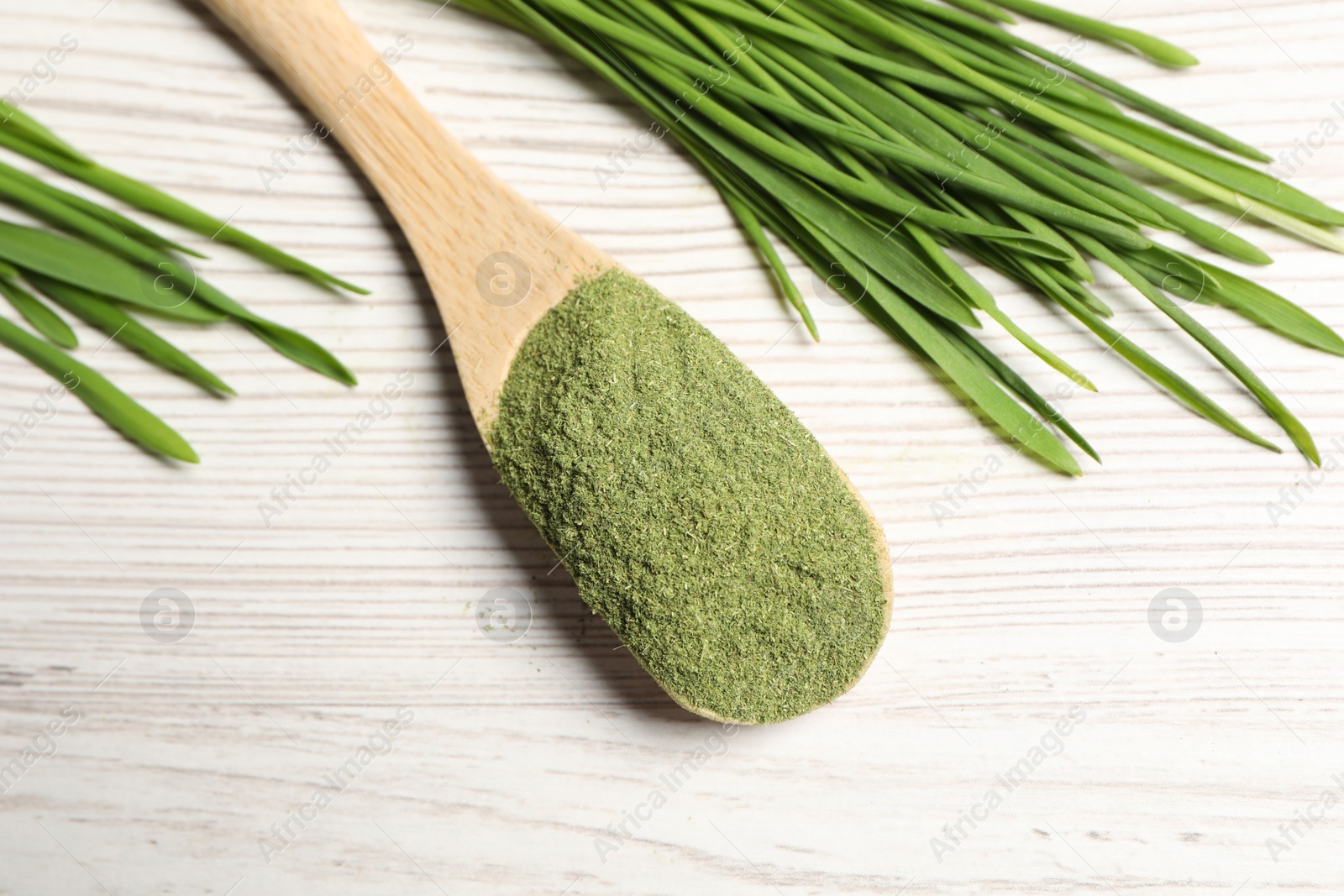 Photo of Wheat grass powder in spoon and fresh sprouts on white wooden table, above view