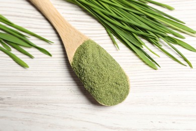 Wheat grass powder in spoon and fresh sprouts on white wooden table, above view