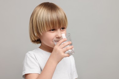 Photo of Cute little boy drinking fresh water from glass on light grey background, space for text