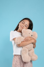 Photo of Cute girl wearing pajamas with teddy bear on light blue background