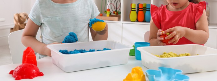 Cute little children playing with bright kinetic sand at table in room, closeup. Banner design