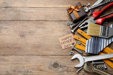 Photo of Card with phrase HAPPY FATHER'S DAY and different tools on wooden background, flat lay. Space for text
