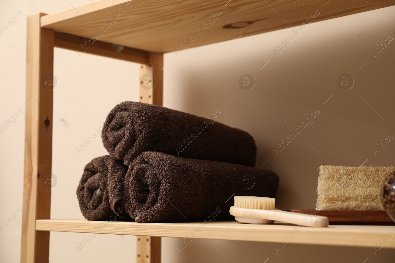 Photo of Soft towels, brush and loofah on wooden shelf indoors, closeup