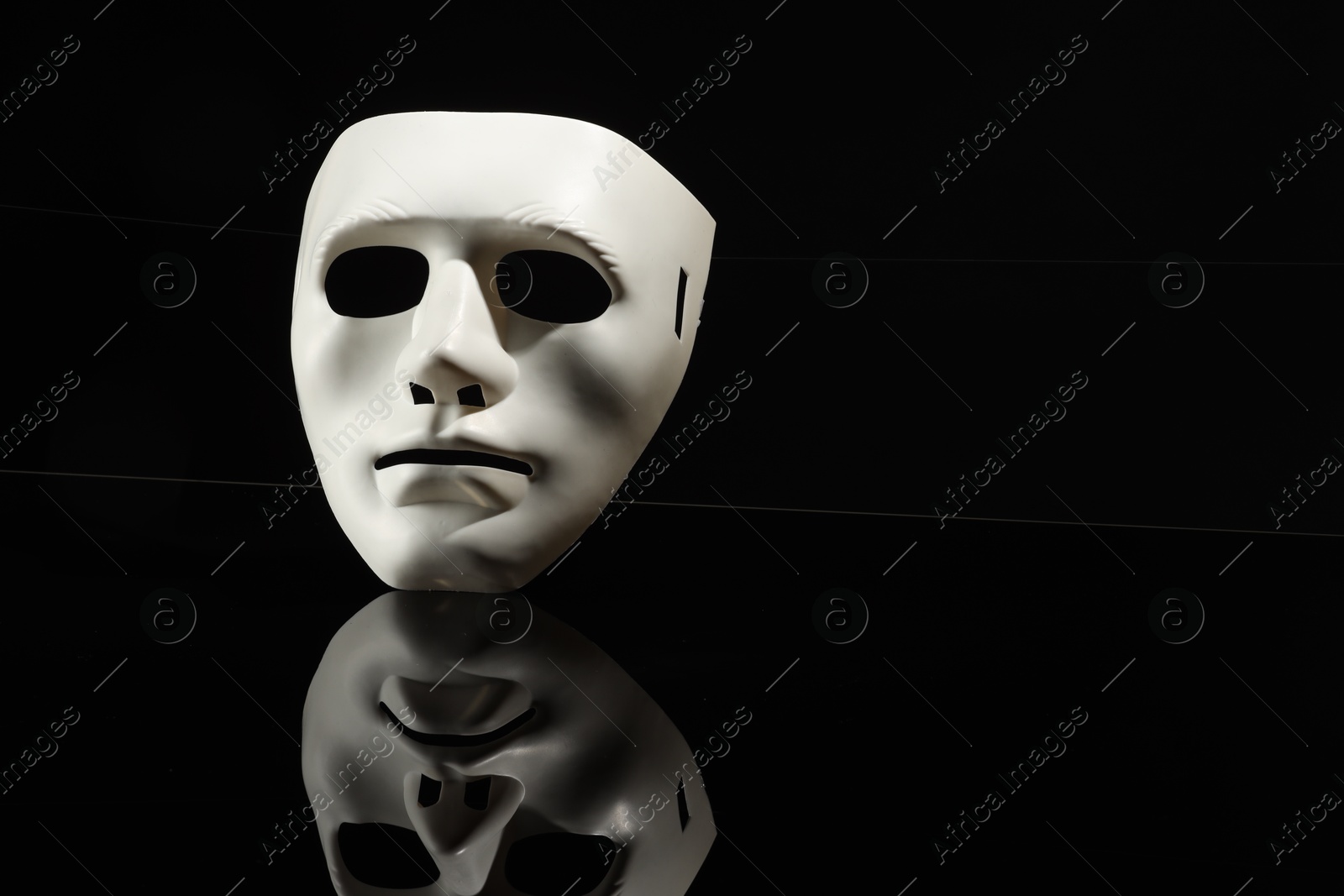 Photo of Plastic face mask on black mirror surface, space for text. Theatrical performance