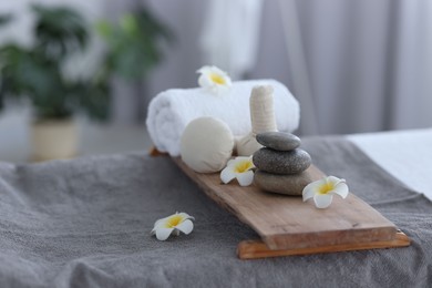 Photo of Stacked spa stones, flowers, herbal bags and towel on massage table indoors