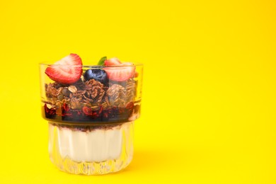 Photo of Tasty granola with berries, jam and yogurt in glass on yellow background, space for text