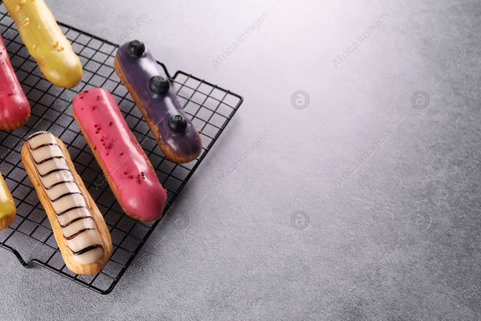 Photo of Cooling rack with different tasty glazed eclairs on grey table, above view. Space for text