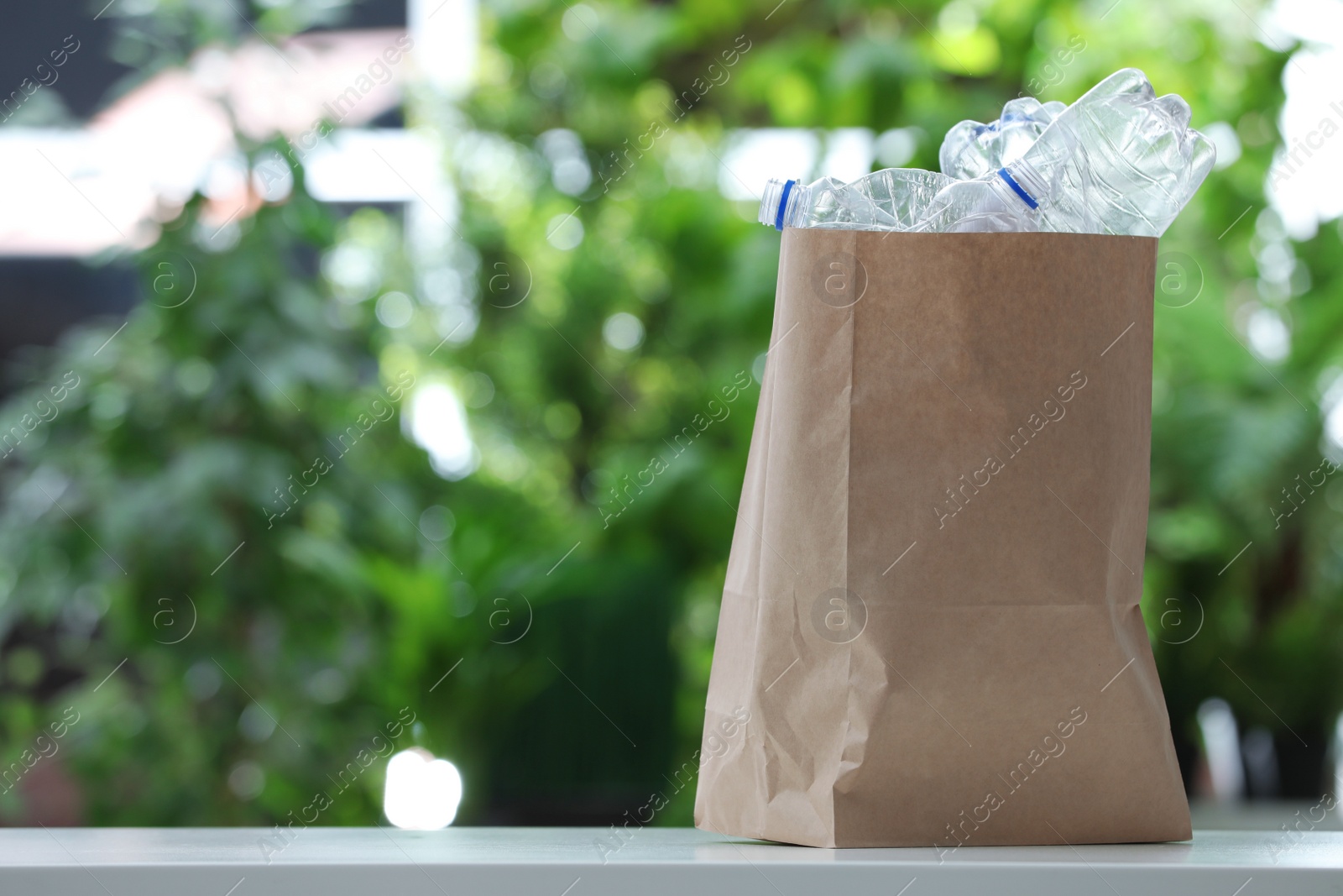 Photo of Used plastic bottles in paper bag on blurred background, space for text. Recycling problem