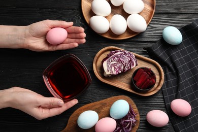 Photo of Woman holding Easter egg painted with natural dyes at black wooden table, top view. Beetroot used for coloring