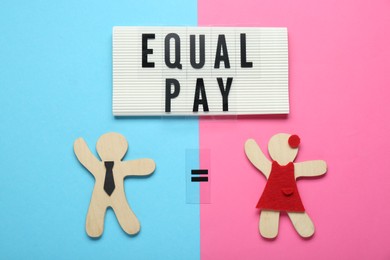 Photo of Equal pay concept. Wooden figures of man and woman on color background, flat lay