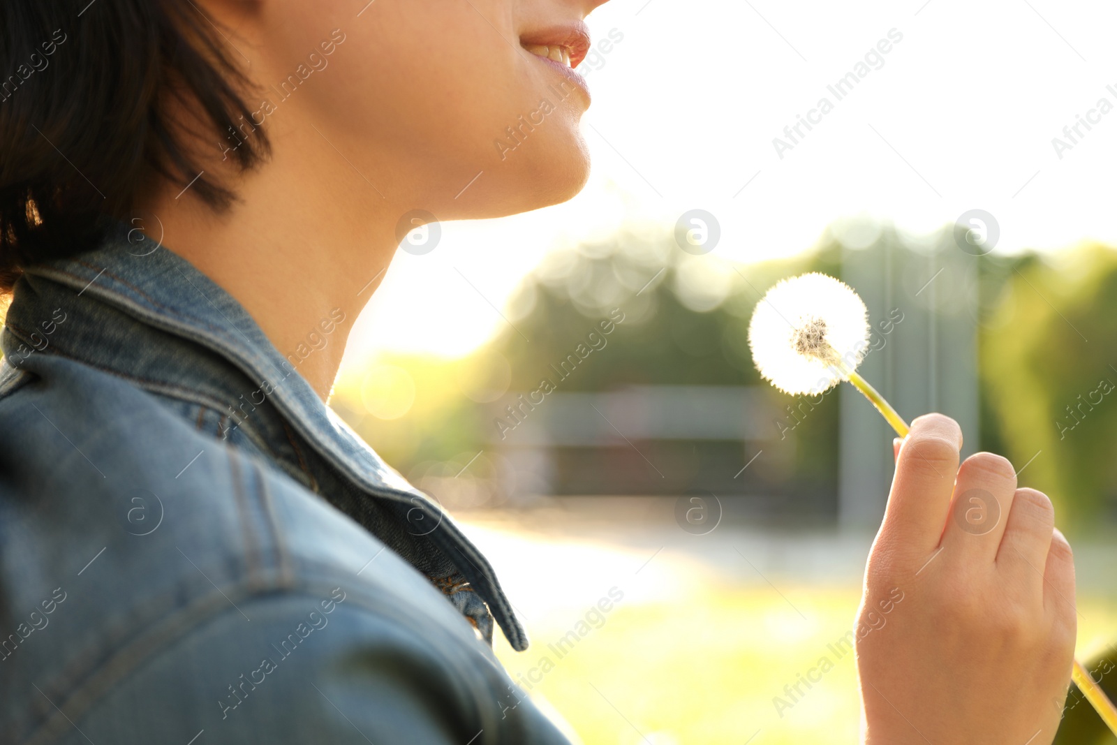 Photo of Young woman with dandelion in park on sunny day, closeup. Allergy free concept