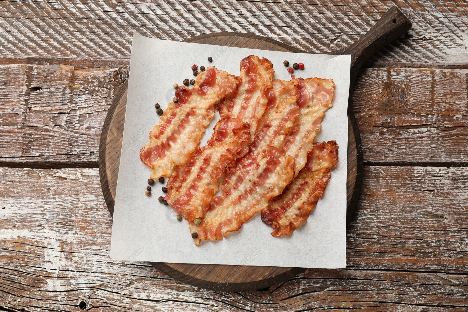 Photo of Delicious fried bacon slices on wooden table, top view