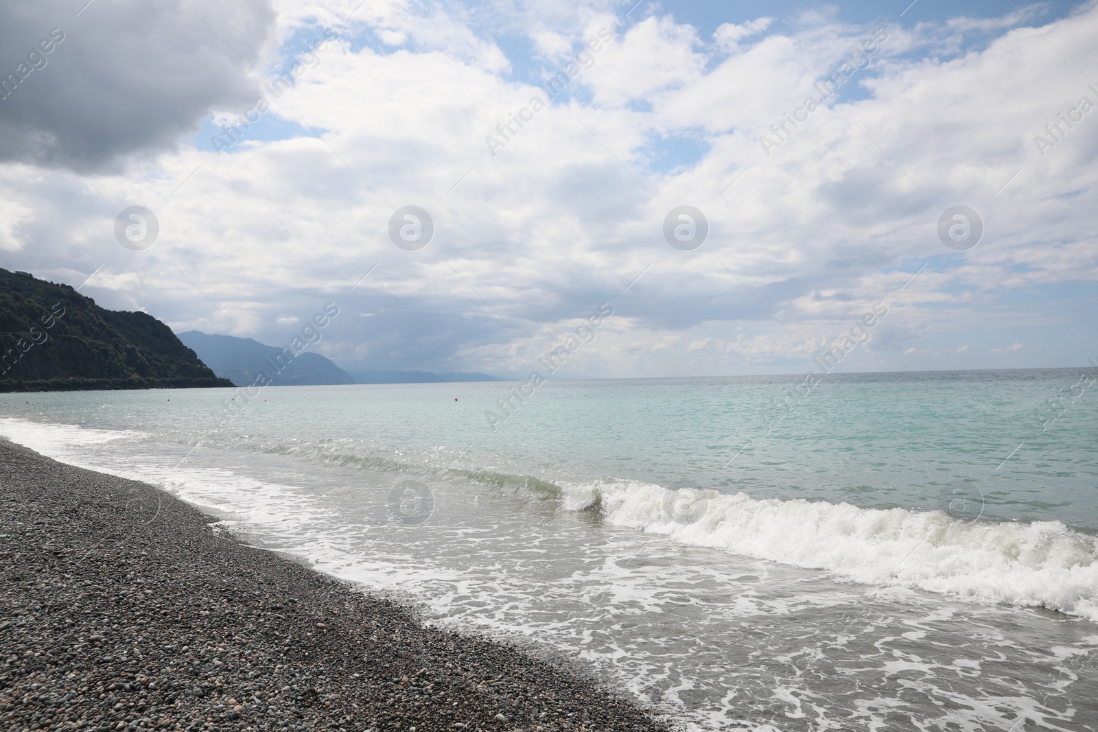 Photo of Picturesque view of beautiful sea shore and hills under sky with fluffy clouds