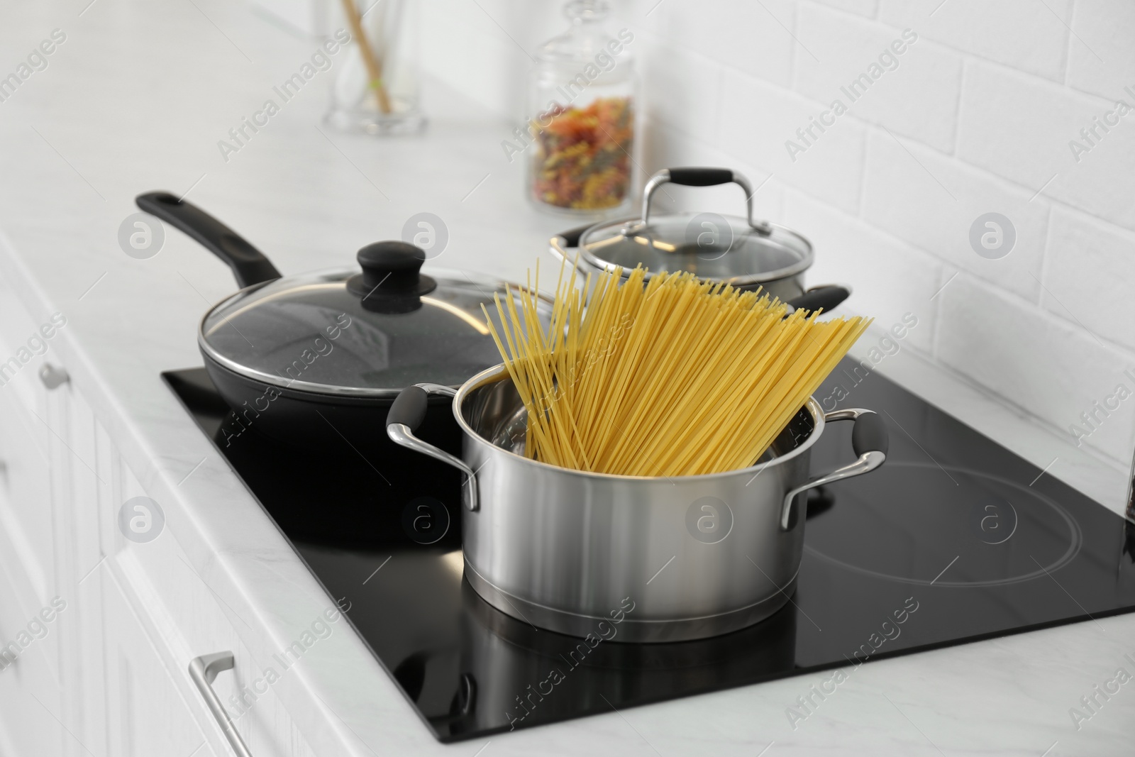 Photo of Pot with uncooked pasta and frying pan on stove in kitchen