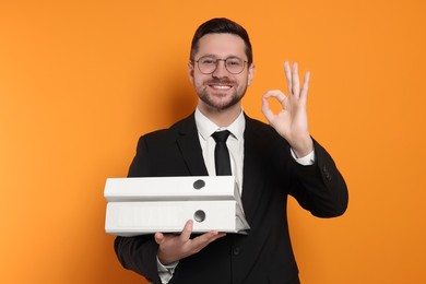 Happy accountant with folders showing ok gesture on orange background