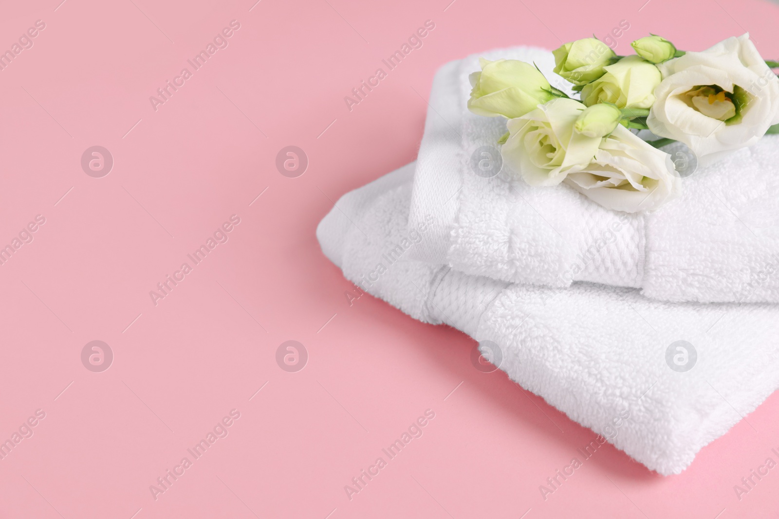 Photo of Soft folded white towels with flowers on violet background, space for text