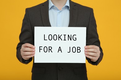 Photo of Unemployed man holding sign with phrase Looking For A Job on orange background, closeup