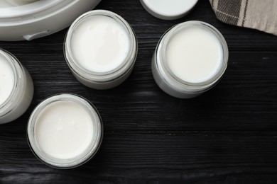 Photo of Tasty yogurt in glass jars on black wooden table, flat lay