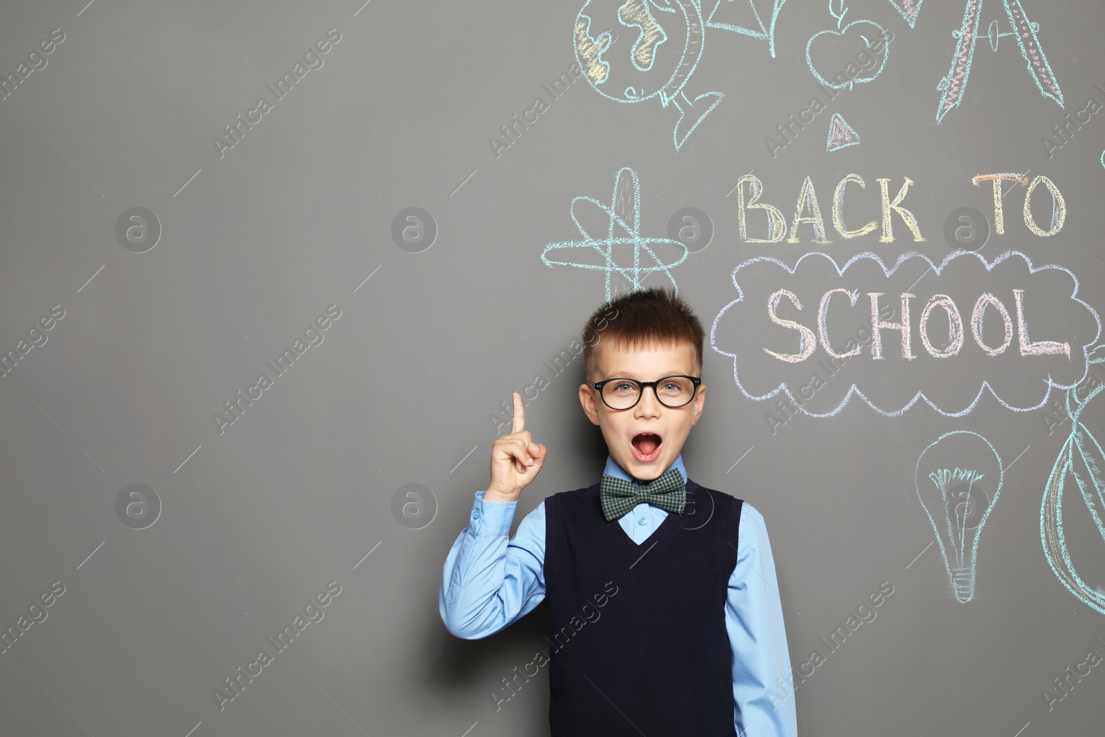 Photo of Little child in uniform near drawings with text BACK TO SCHOOL on grey background