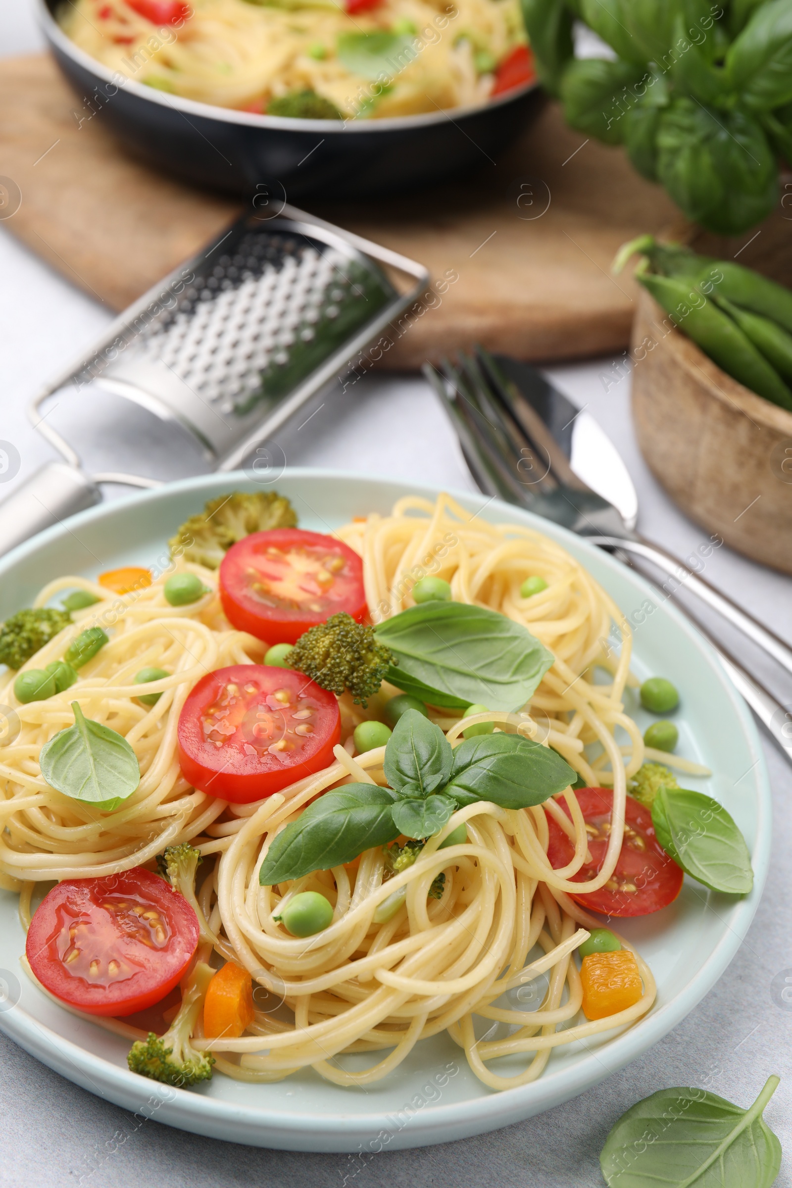 Photo of Delicious pasta primavera, ingredients and cutlery on light gray table, closeup