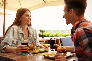 Young happy couple with burgers in street cafe