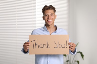 Photo of Happy man holding cardboard sheet with phrase Thank You indoors