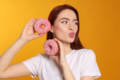 Photo of Beautiful woman with red dyed hair and donuts blowing kiss on orange background