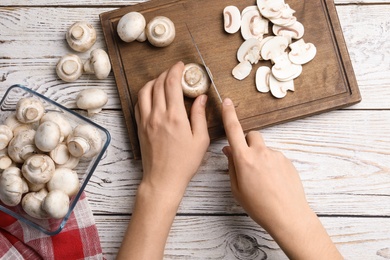 Photo of Woman cutting fresh raw mushrooms on wooden table, top view