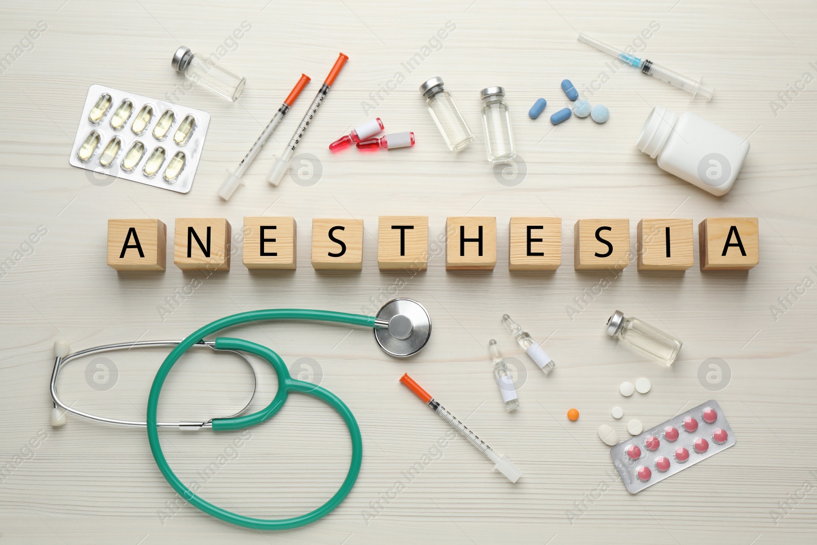 Photo of Word Anesthesia made of cubes, stethoscope and drugs on white wooden table, flat lay