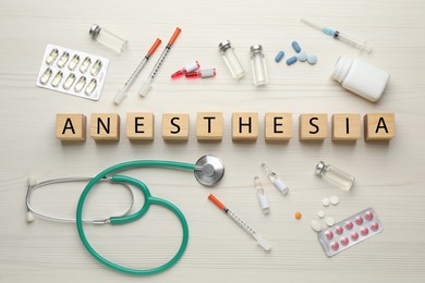 Photo of Word Anesthesia made of cubes, stethoscope and drugs on white wooden table, flat lay