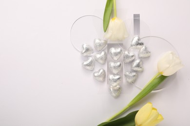 Photo of Heart made with delicious chocolate candies and beautiful tulips on white background, top view. Space for text