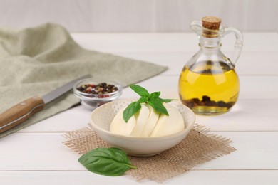 Photo of Tasty mozzarella slices and basil leaves on white wooden table