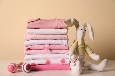 Stack of baby girl's clothes, rattles, pacifier and toy bunny on white table