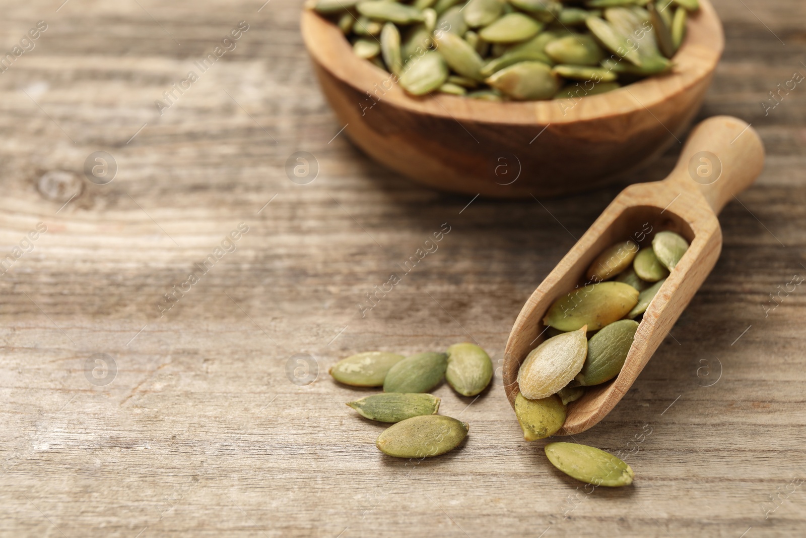 Photo of Scoop and bowl with peeled pumpkin seeds on wooden table, closeup. Space for text