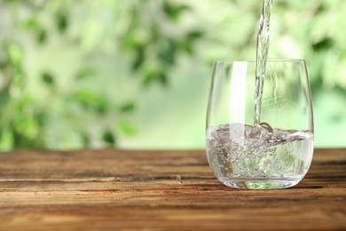 Pouring water into glass on wooden table outdoors, space for text. Refreshing drink