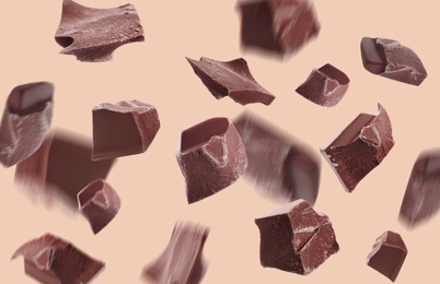 Delicious chocolate pieces falling on beige background