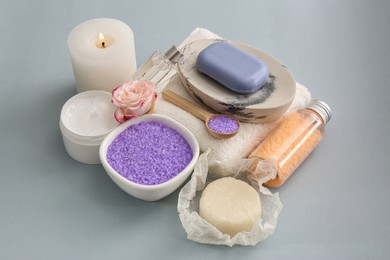 Sea salt, burning candle and spa products on light grey background