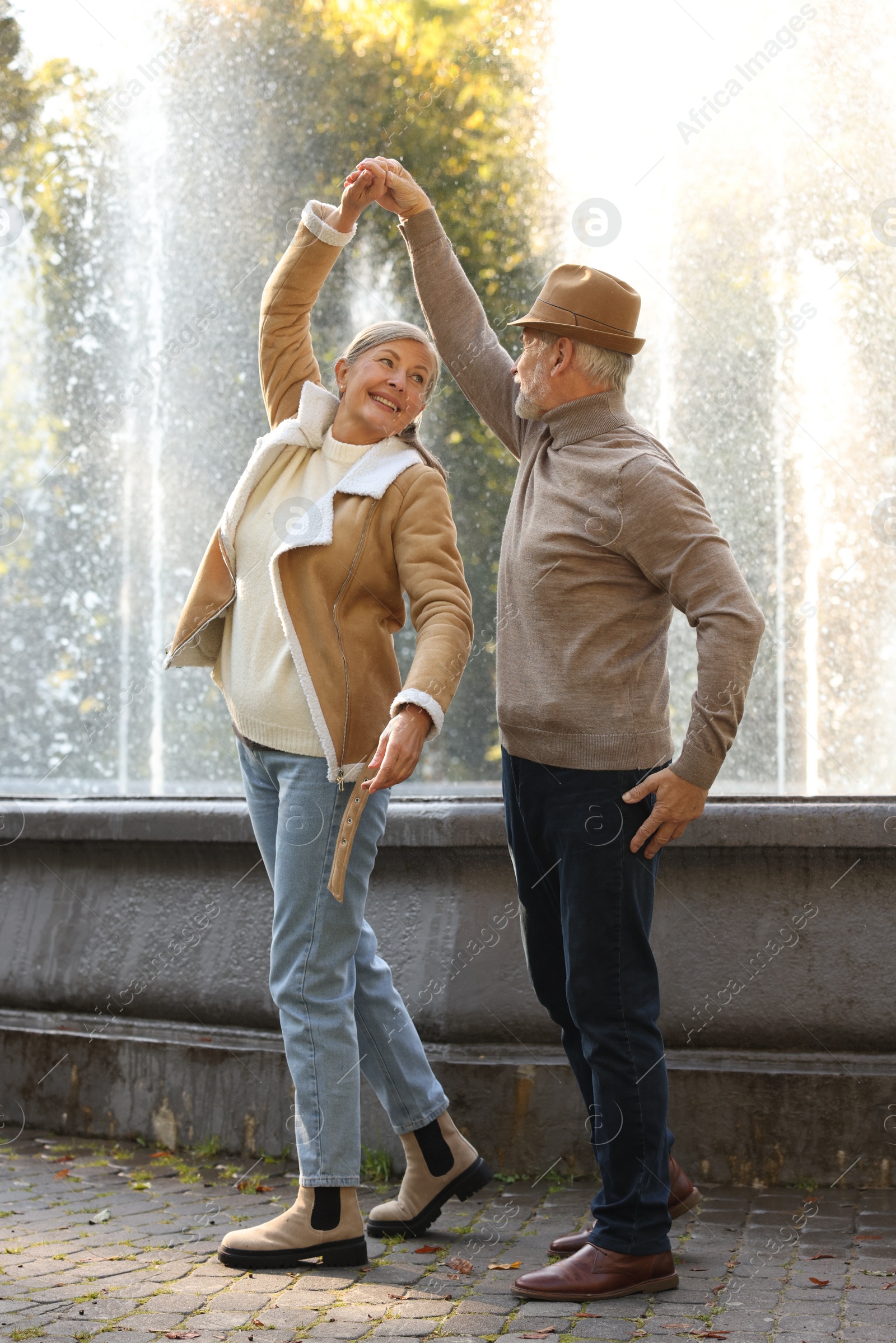 Photo of Affectionate senior couple dancing together near fountain outdoors