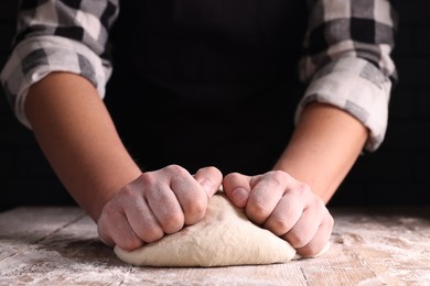 Photo of Man kneading dough at wooden table on dark background, closeup