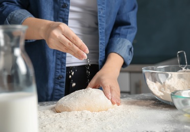 Photo of Woman sprinkling flour over dough on table in kitchen