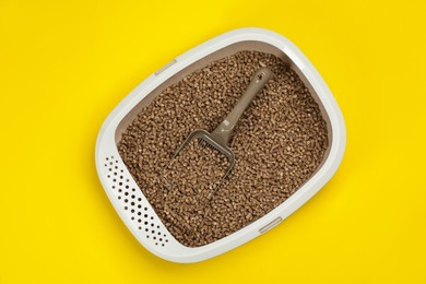 Cat litter tray with filler and scoop on yellow background, top view
