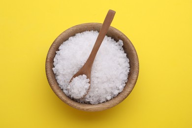 Photo of Bowl and spoon with sea salt on yellow background, top view