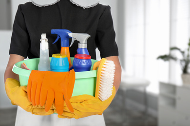 Image of Young chambermaid holding plastic basin with detergents in office, closeup
