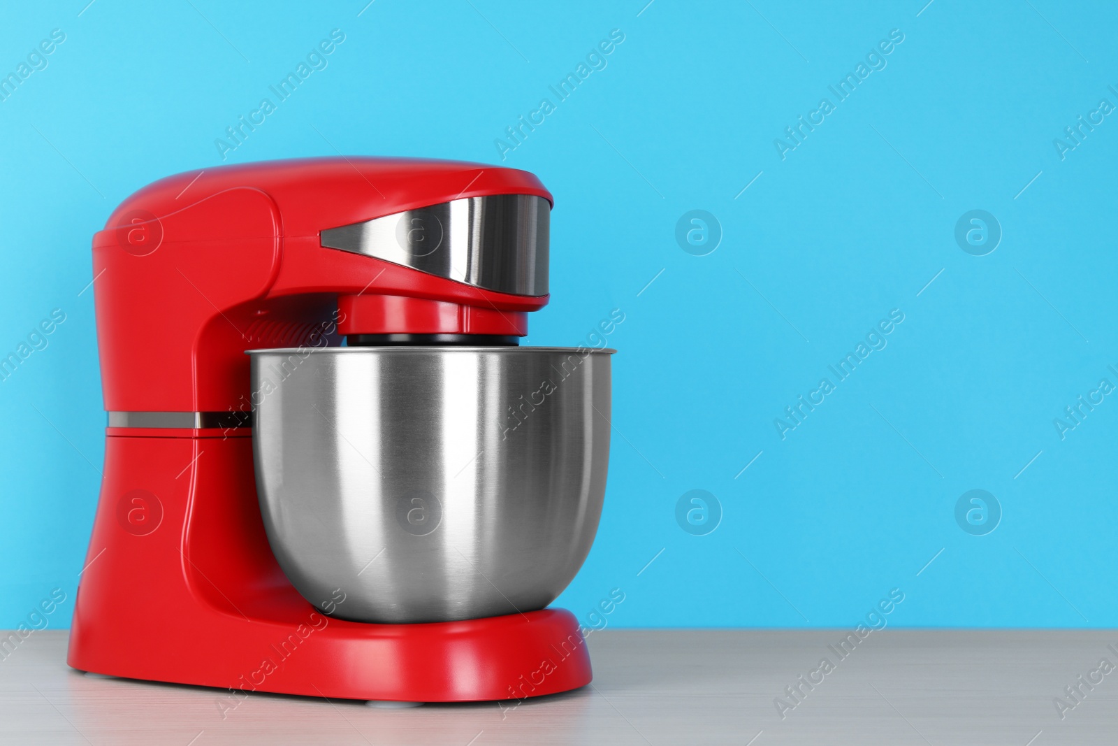 Photo of Modern red stand mixer on white wooden table against turquoise background, space for text