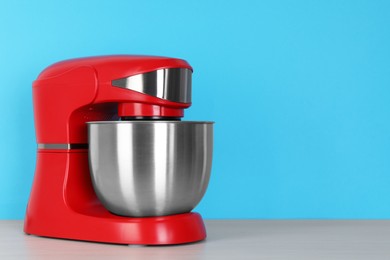 Photo of Modern red stand mixer on white wooden table against turquoise background, space for text