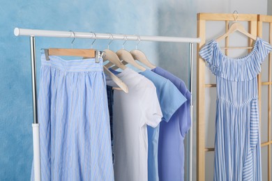 Rack with stylish clothes near light blue wall indoors