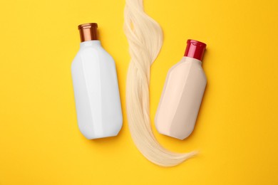Photo of Lock of hair and shampoo bottles on yellow background, flat lay