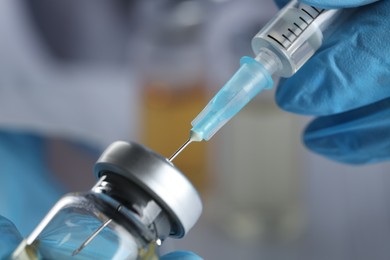 Doctor filling syringe with medication from glass vial, closeup