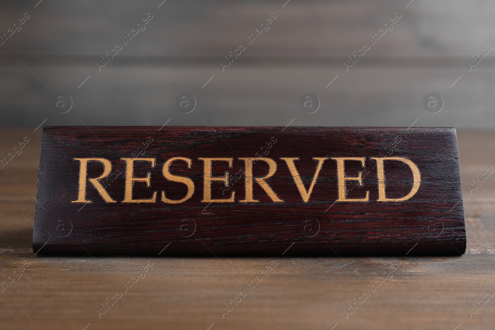 Photo of Elegant sign RESERVED on wooden surface. Table setting element